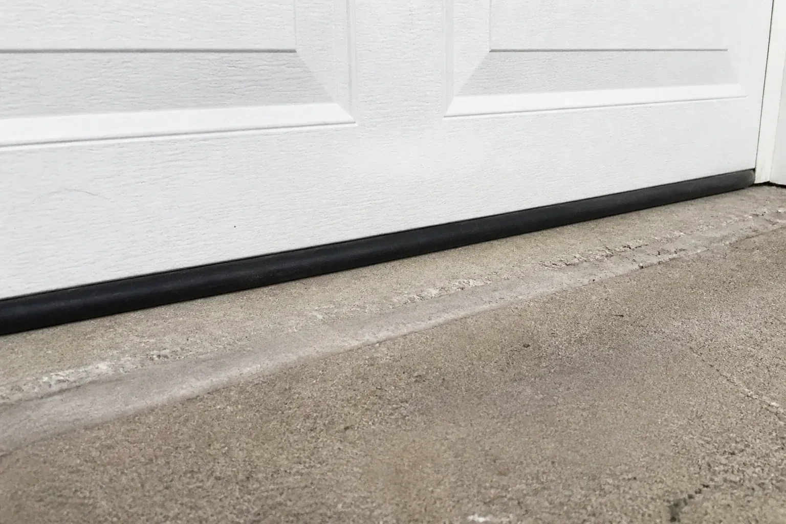 Black bottom seal along a closed white garage door at a concrete threshold. — Garage Door Bottom Seal Replacement, Richmond Hill