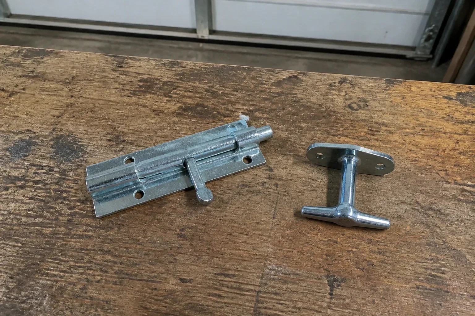 Detached slide bolt and T-handle on a wooden garage workbench. — Garage Door Manual Lock Repair, Richmond Hill