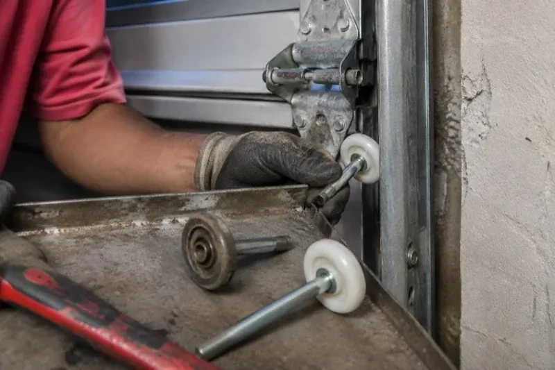 Gloved hand holding a white garage-door roller beside its track, with two loose rollers and a red tool on a tray. — Garage Door Roller Replacement, Richmond Hill